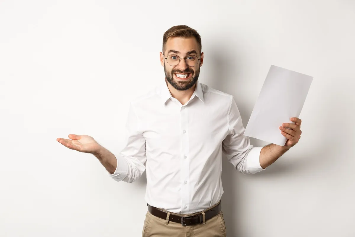 Homem de óculos e barba, vestindo camisa social branca, segura um documento com expressão de dúvida, ilustrando incerteza sobre carta de crédito sem anuidade.
