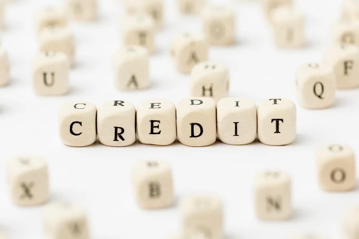 Cubos de madeira dispostos em sequência formando a palavra "CREDIT" sobre uma superfície branca, representando o conceito de crédito e financiamento.