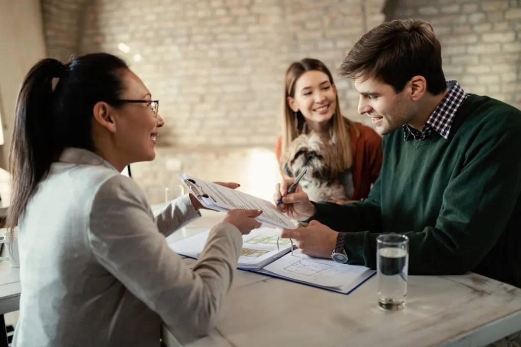 Casal sorridente assinando contrato com uma consultora imobiliária, demonstrando satisfação na aquisição de um novo imóvel.