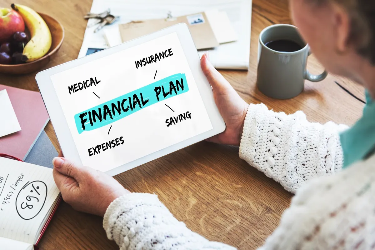 Pessoa segurando um tablet com um diagrama de planejamento financeiro, destacando áreas como despesas, economia, seguro e saúde.