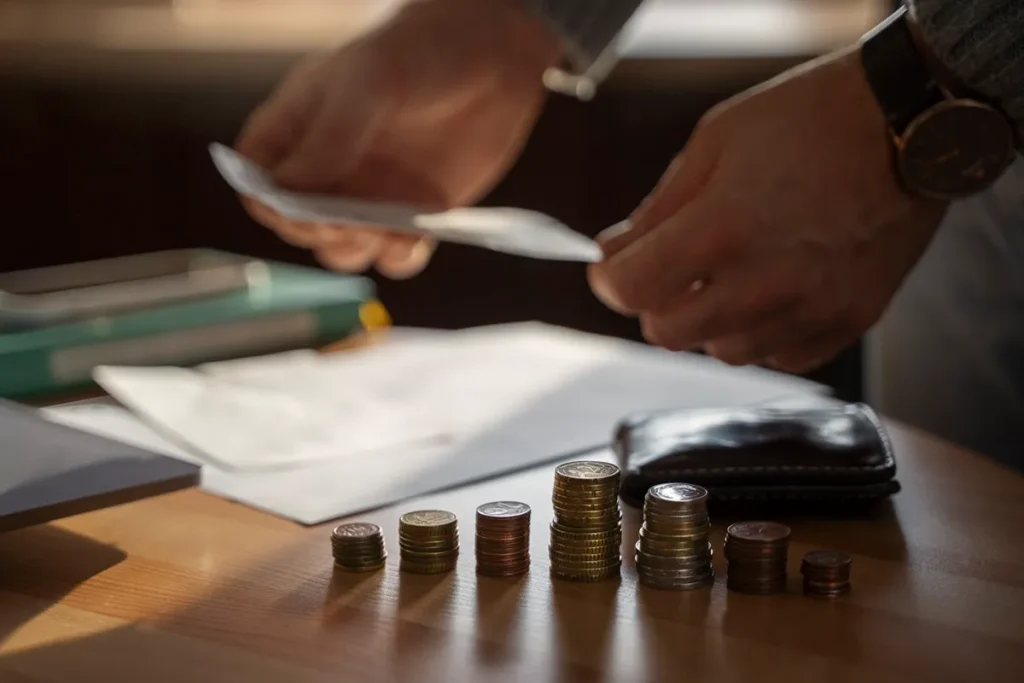 Pessoa organizando documentos e contando moedas empilhadas sobre a mesa, representando controle financeiro