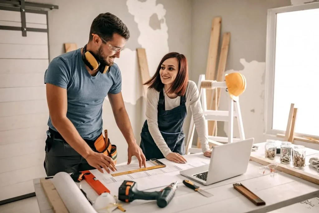 Casal planejando reforma de casa com ferramentas, laptop e projeto sobre a mesa, representando consórcio para reforma.