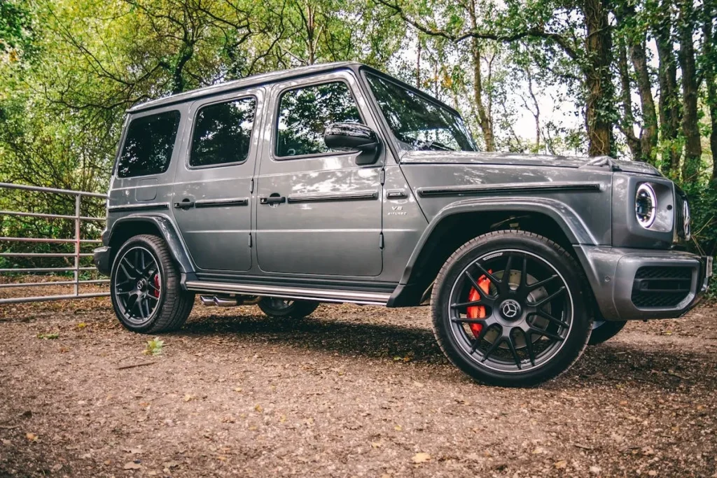 Um carro cinza, modelo SUV G-Class da Mercedes-Benz, com rodas esportivas e pinças de freio vermelhas. A imagem destaca um veículo seminovos em um ambiente natural.