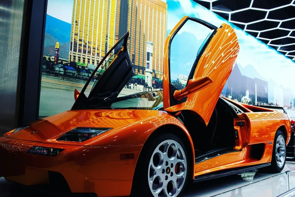 Um carro de luxo laranja, modelo Lamborghini Diablo, com portas estilo tesoura abertas, exibido em um showroom.