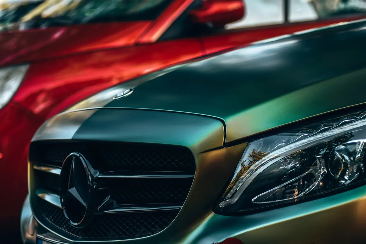 Mercedes-Benz com pintura de efeito gradiente, destacando sua grade frontal e faróis detalhados, estacionado ao lado de um carro vermelho