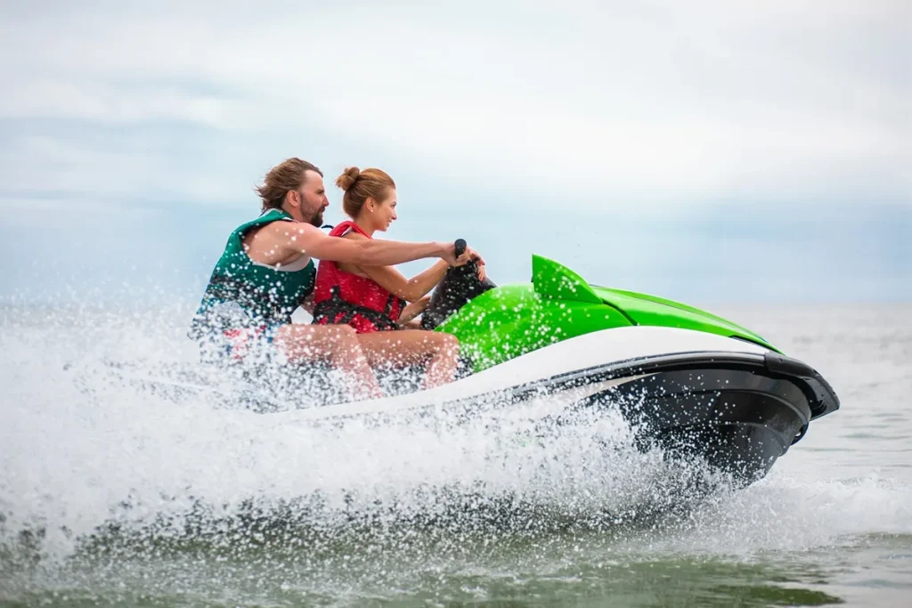 Casal se divertindo em um jet ski verde e branco, acelerando sobre as águas do mar.