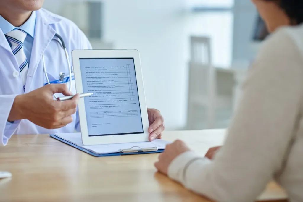 Imagem de um médico mostrando um formulário eletrônico em um tablet para um paciente, enquanto aponta para as perguntas do formulário.