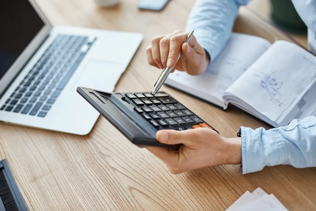Pessoa calculando projeções financeiras com calculadora, caderno de anotações e notebook, representando análise da taxa SELIC.