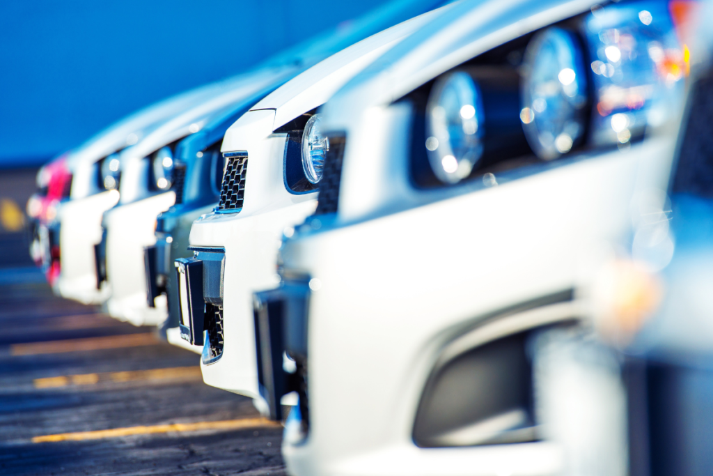 Fileira de carros novos estacionados em uma concessionária, com foco nos faróis e grades frontais.