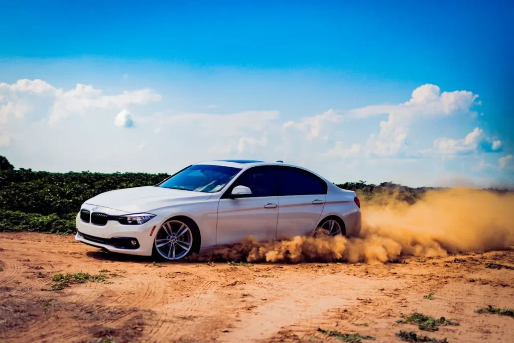 Carro sedan branco de luxo derrapando em estrada de terra com poeira ao fundo em dia ensolarado