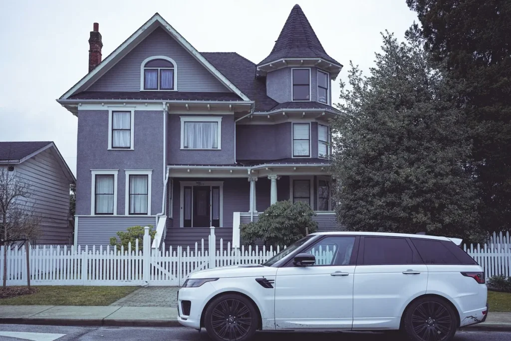 Casa vitoriana com carro de luxo branco estacionado em frente e cerca branca ao redor