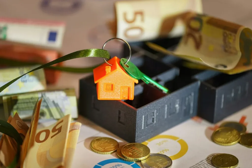 Chave com miniatura de casa laranja sobre maquete de imóvel, notas e moedas de euro ao redor, representando carta de crédito imobiliário