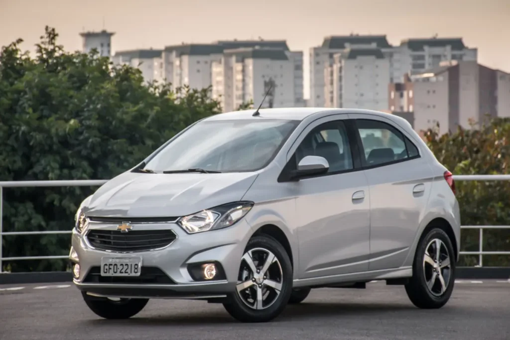 Chevrolet Onix prata estacionado em área urbana com prédios ao fundo.