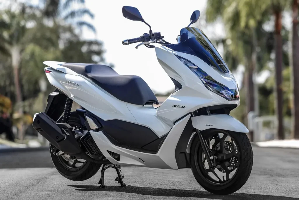 Moto Honda PCX branca estacionada ao ar livre com fundo de árvores, destacando seu design elegante e urbano