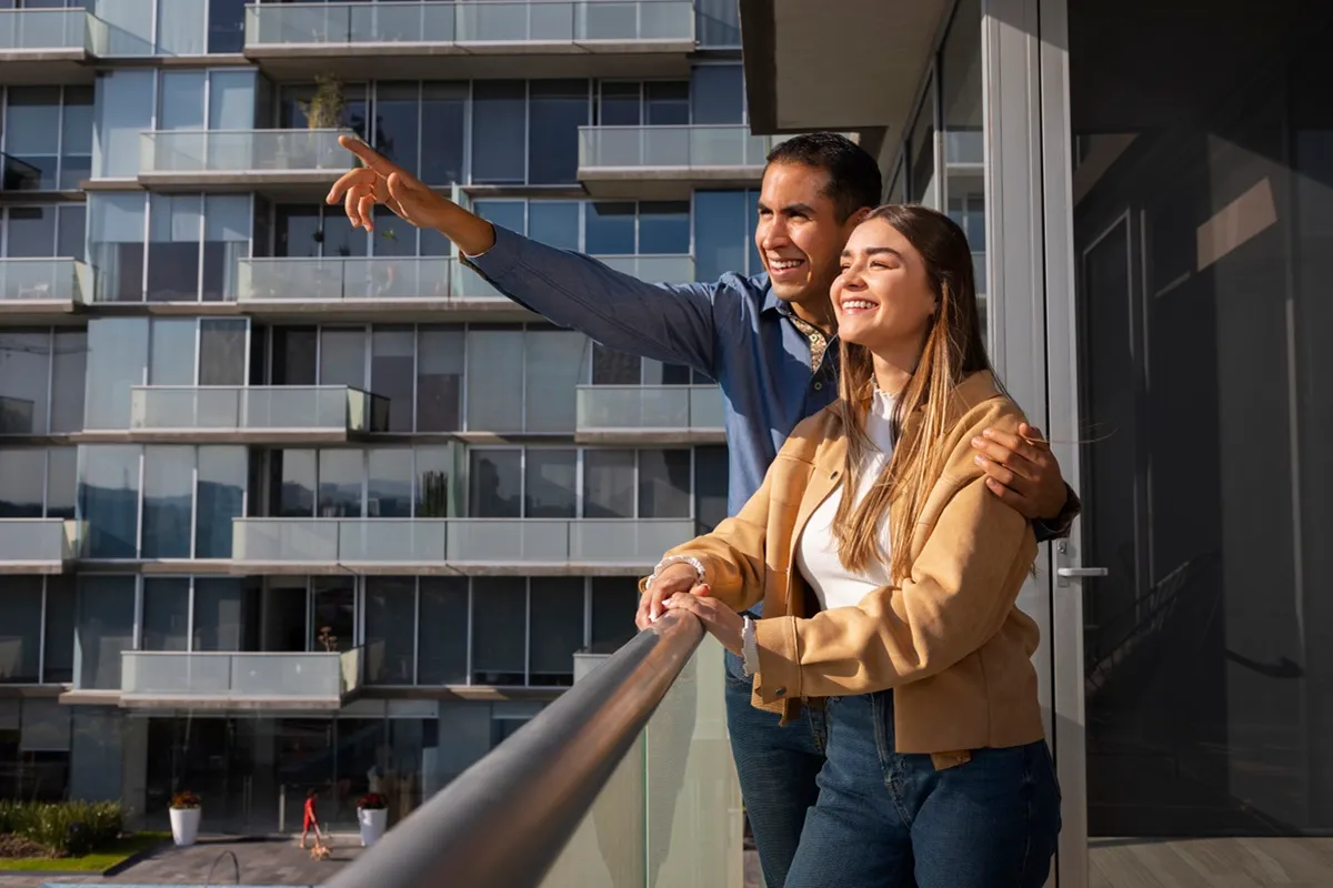Casal feliz de mãos dadas observando o apartamento moderno na varanda.