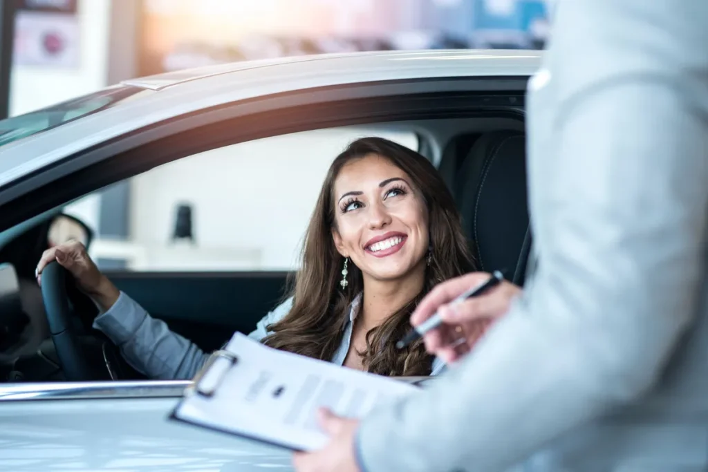 Mulher sorridente dentro de carro novo assinando contrato de consórcio em concessionária.
