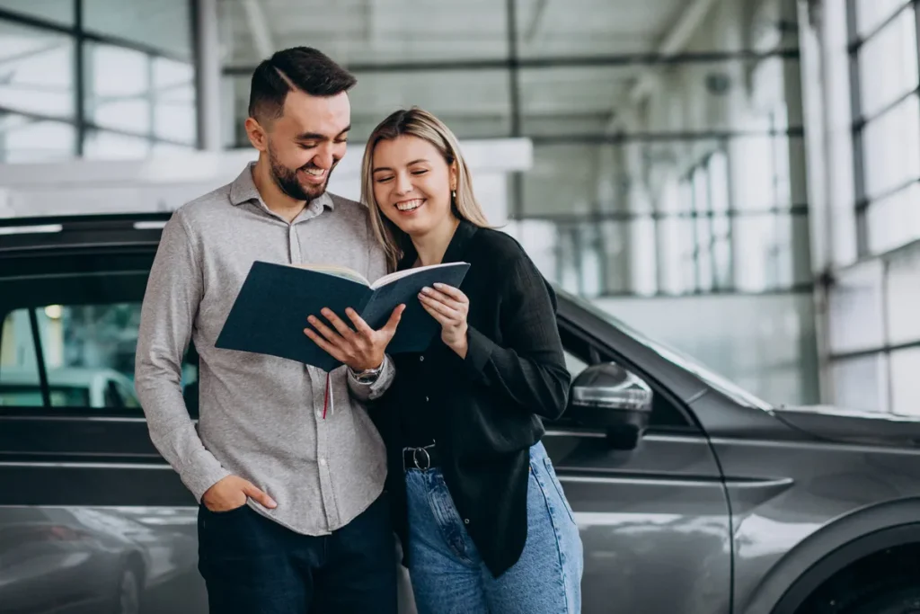 Casal sorridente analisando contrato de consórcio de carro em concessionária.