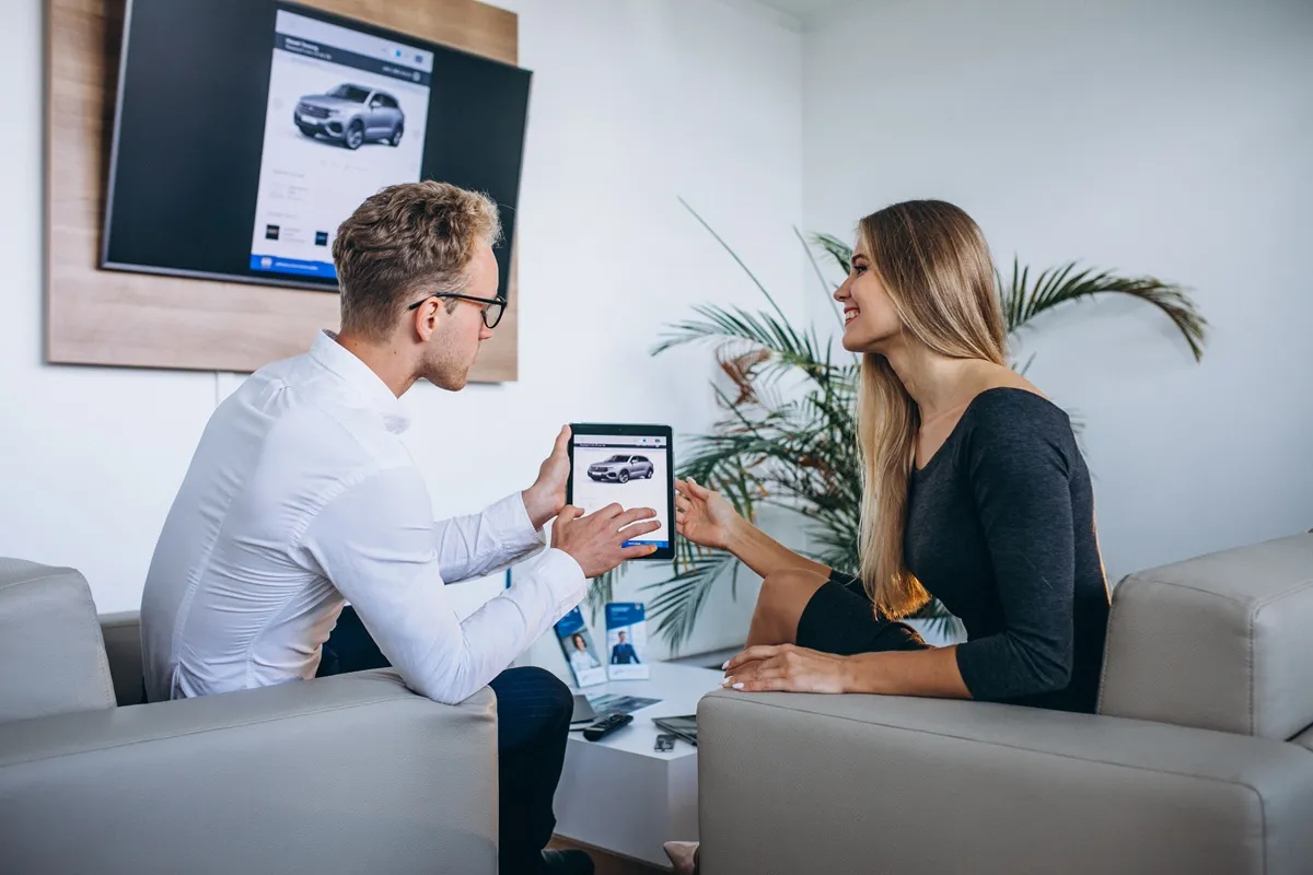 Vendedor e cliente discutindo detalhes de um consórcio de carros enquanto visualizam uma simulação de veículo em um tablet, em ambiente moderno de escritório