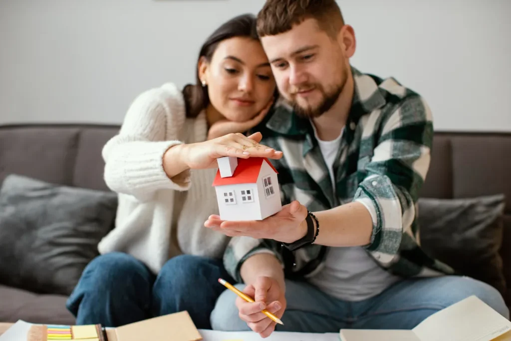 Casal segurando uma miniatura de casa, representando planejamento para compra de imóvel ou consórcio imobiliário