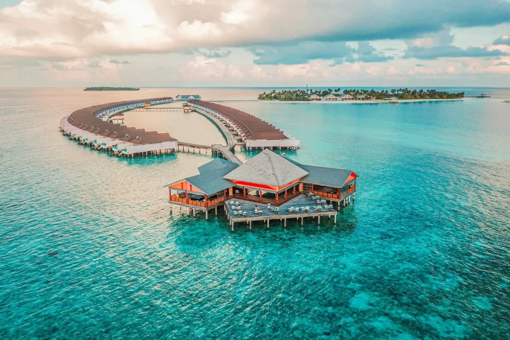 Vista aérea de resort de luxo com bangalôs sobre o mar cristalino nas Maldivas, ao pôr do sol