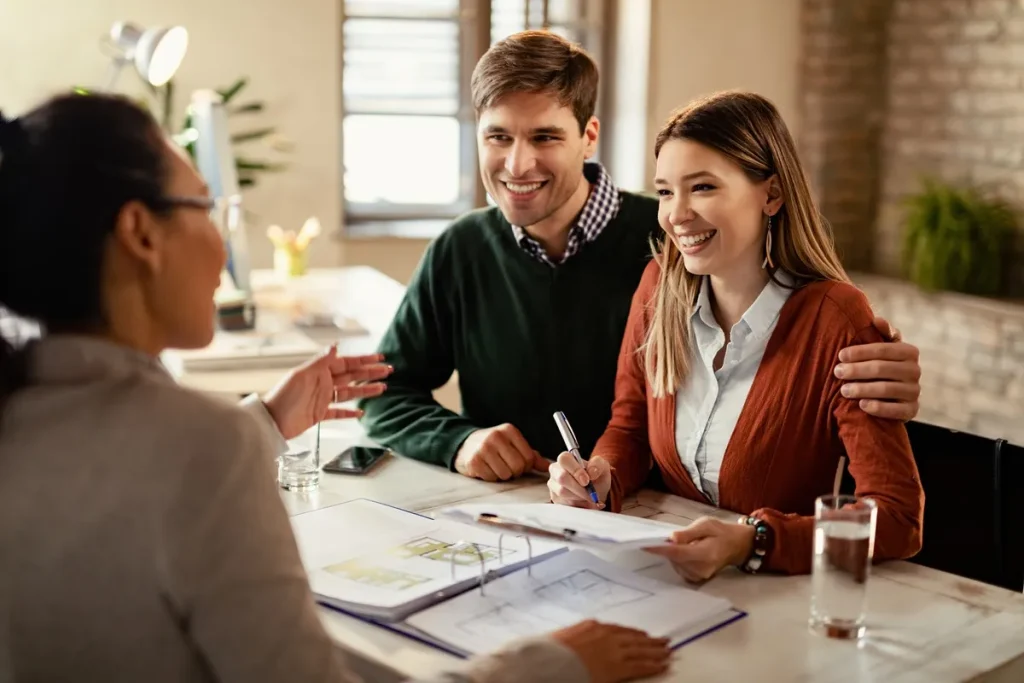 Casal sorridente assina documentos de consórcio imobiliário enquanto conversa com consultora financeira em um escritório claro e acolhedor