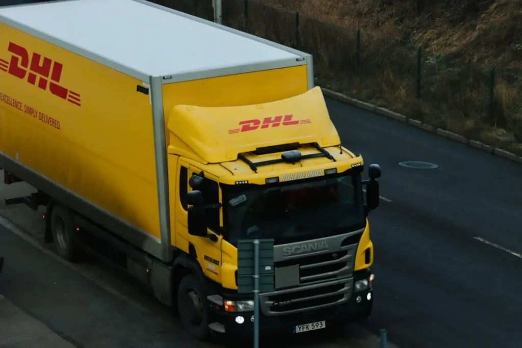Um camião de entregas amarelo e branco com o logótipo da DHL, a representar a chegada de um bem e a contemplação num consórcio.