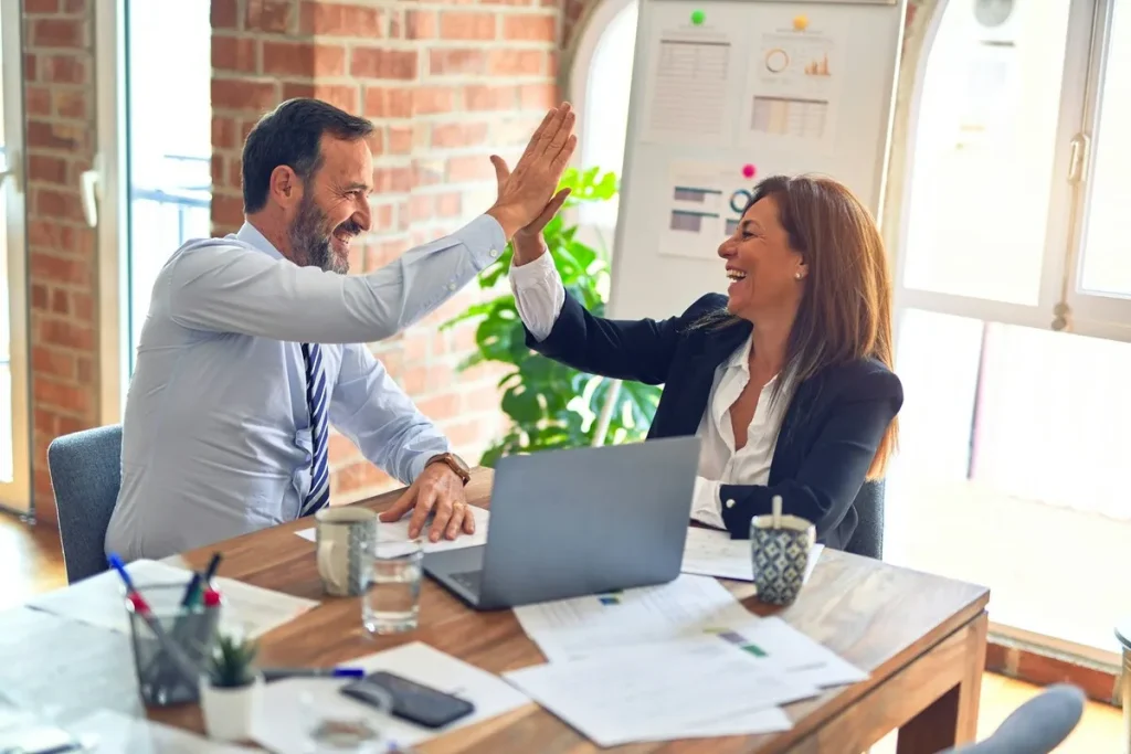 Dois colegas de trabalho comemorando com um high five em escritório moderno