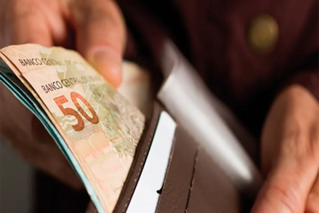 Pessoa retirando nota de 50 reais de uma carteira de couro.