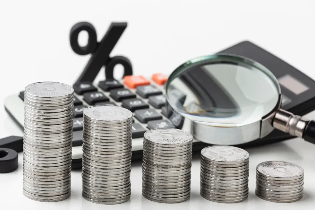 Moedas empilhadas representando valores financeiros, com uma lupa e calculadora ao fundo, simbolizando a análise da inadimplência e finanças pessoais.