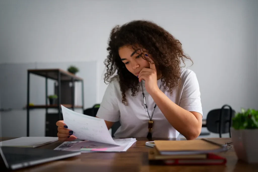 Jovem mulher sentada em mesa analisando documentos, representando o tema de inadimplência e problemas financeiros.