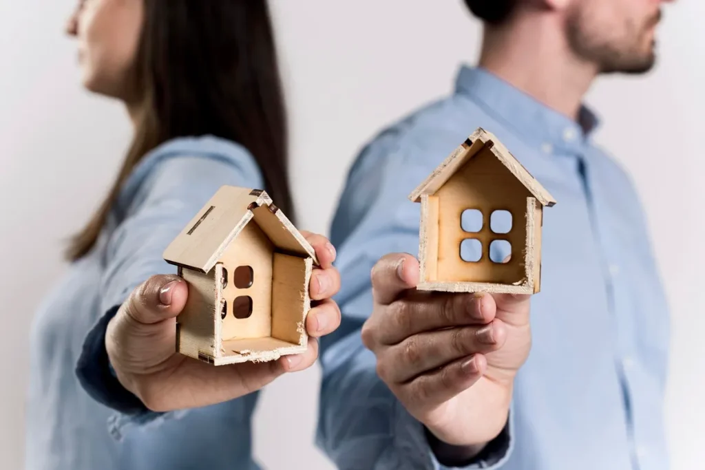 Imagem mostrando duas pessoas segurando modelos de casas de madeira, representando a troca de imóveis
