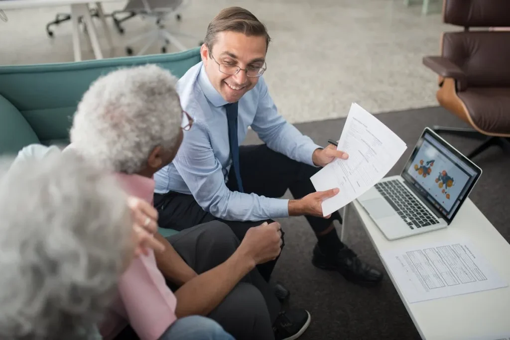 Consultor financeiro explicando documentos de investimento para casal de idosos com gráficos no notebook