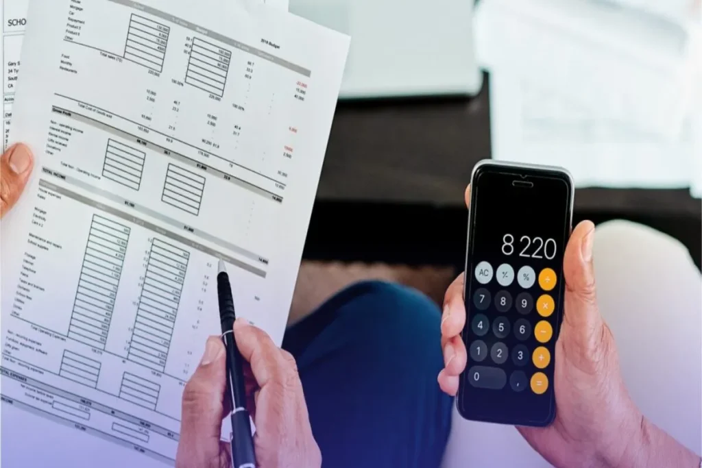 Pessoa analisando planilha de orçamento e usando calculadora no celular para controle financeiro