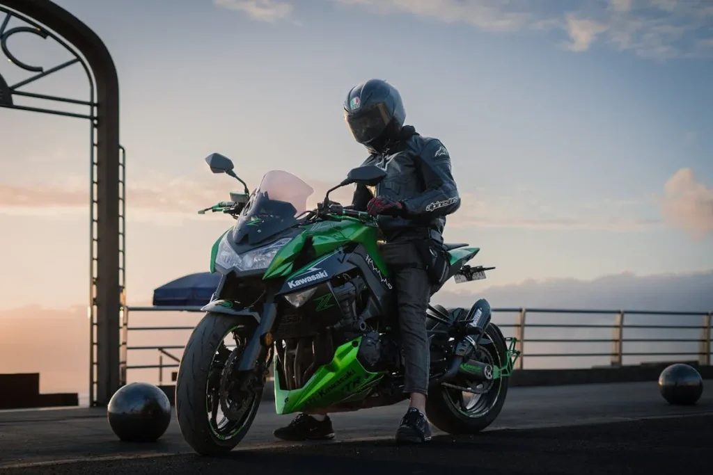 Uma pessoa de capacete e roupa de motociclista sentada em uma potente moto Kawasaki verde e preta, com o sol se pondo no horizonte, sugerindo liberdade e paixão por motocicletas.