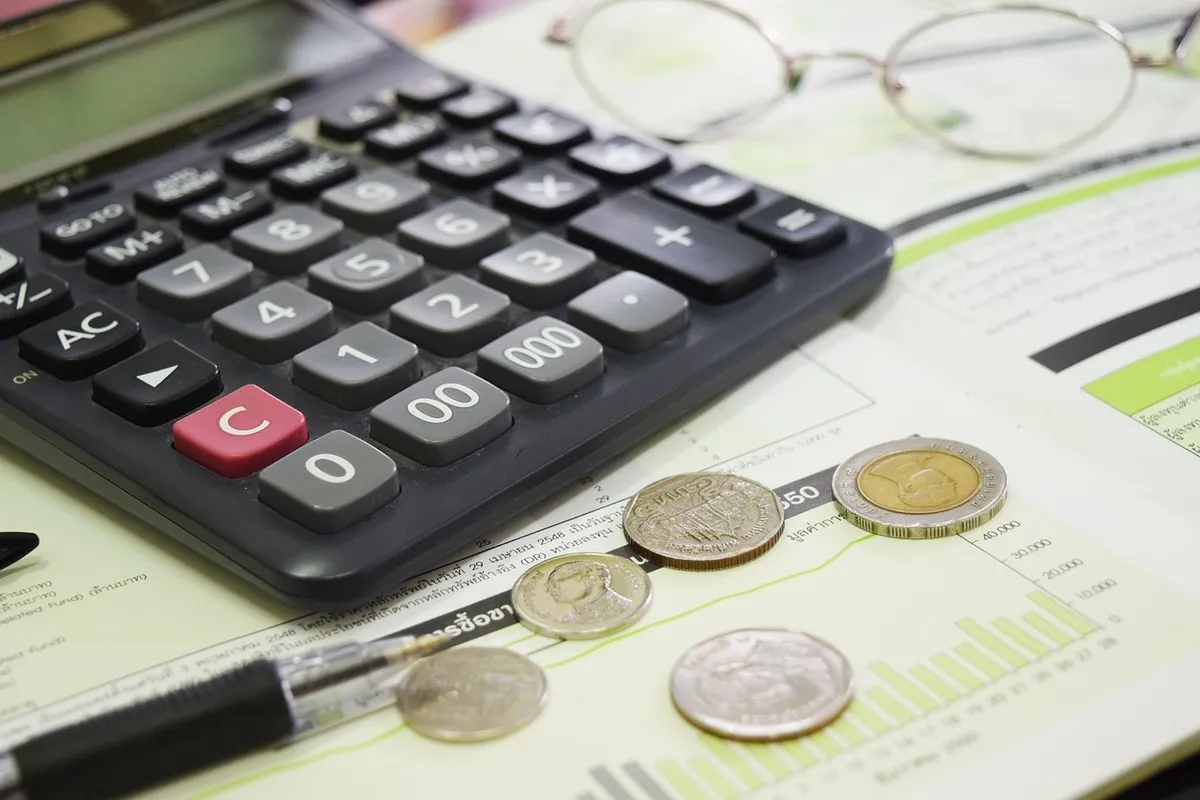 Calculadora, moedas e óculos sobre documentos financeiros, simbolizando o cálculo e impacto do reajuste IPCA.