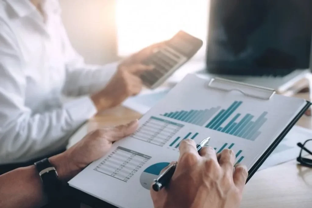 Duas pessoas em uma reunião de negócios, com uma delas segurando um relatório com gráficos e a outra usando uma calculadora, representando o processo de análise de crédito.