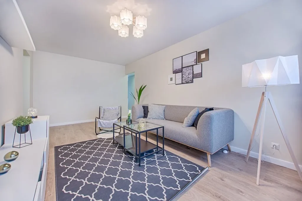 Sala de estar moderna e minimalista, decorada com um sofá cinza, mesa de centro de vidro, luminária de tripé e tapete com estampa geométrica.