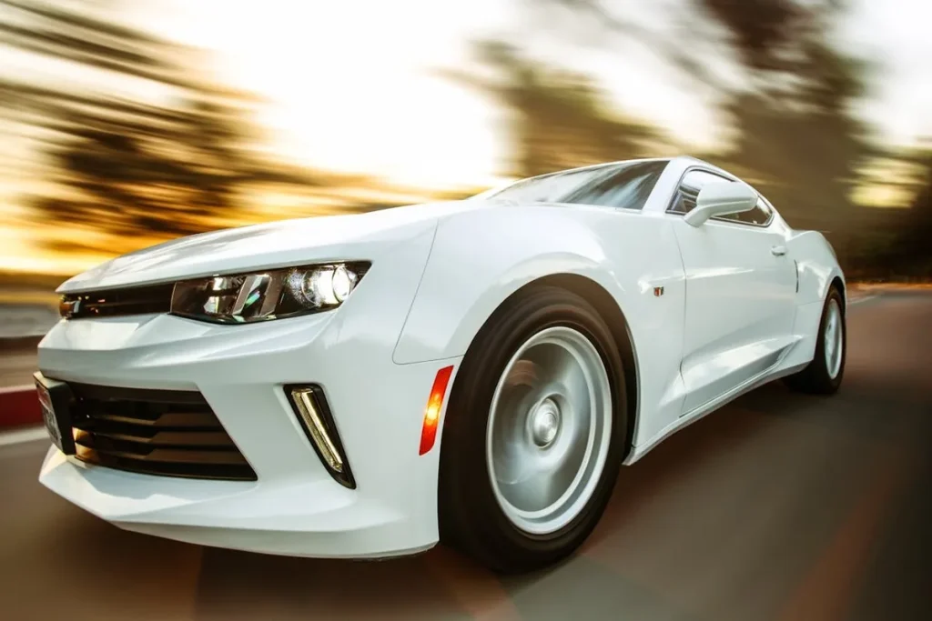 Carro esportivo branco, um Chevrolet Camaro, em alta velocidade, criando um efeito de desfoque de movimento.