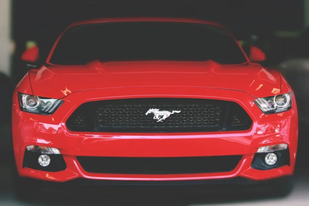 Carro esportivo Ford Mustang vermelho, visto de frente, com o logotipo do cavalo no centro da grade.