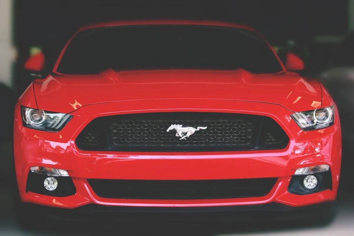Carro esportivo Ford Mustang vermelho, visto de frente, com o logotipo do cavalo no centro da grade.