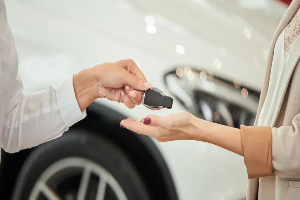 A mão de um vendedor entregando a chave de um carro para um cliente. A imagem representa uma transação de compra, um momento que pode ser financiado com um empréstimo FGTS.