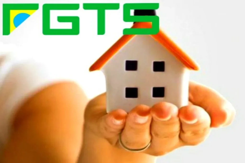 Uma mão segura uma pequena maquete de uma casa branca com telhado laranja. No topo da imagem, a sigla FGTS está em verde, com uma bandeira do Brasil na letra F. A imagem representa o uso do empréstimo FGTS para a compra de um imóvel.