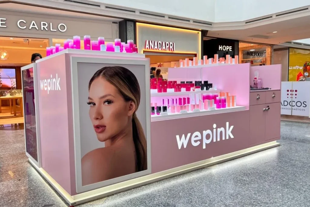 Quiosque de franquia da marca de cosméticos Wepink em um shopping center, exibindo produtos e publicidade.