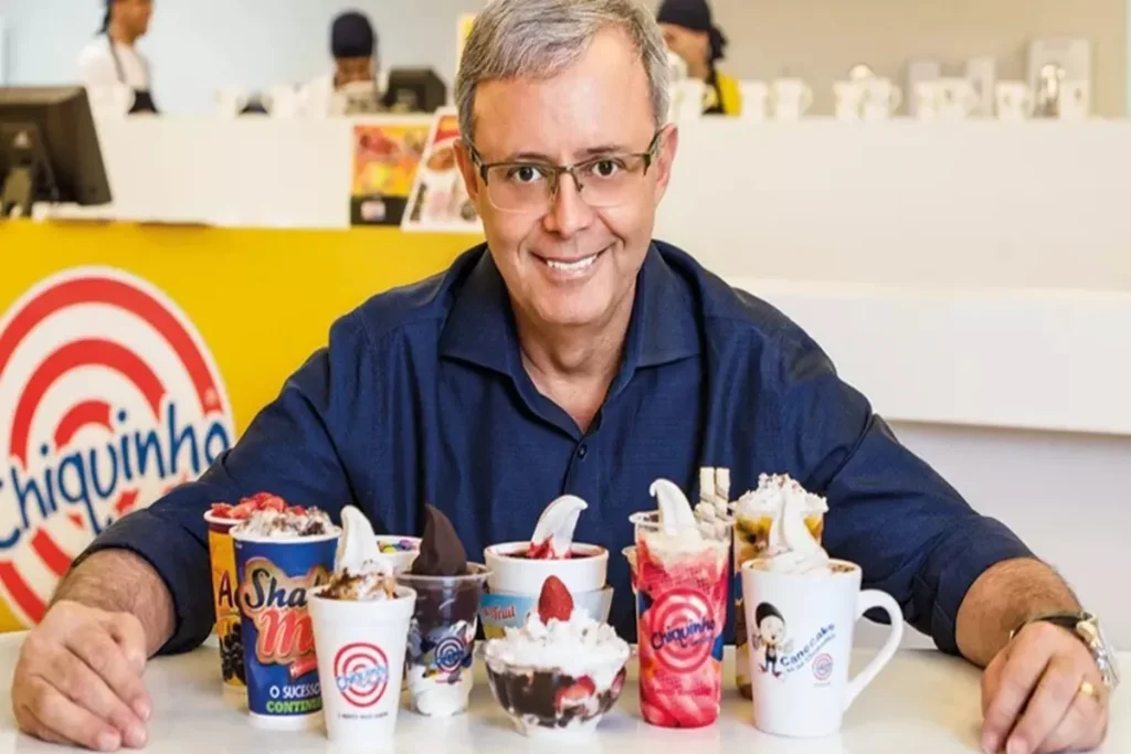 Empresário sorridente em frente a diversos produtos da Chiquinho Sorvetes e Canecake, representando o sucesso e investimento em franquias.