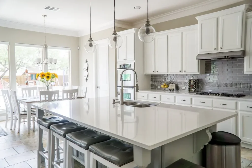 Cozinha de luxo moderna com armários brancos, bancada de mármore e banquetas de couro. A imagem mostra o interior de um imóvel, ideal para locação de imóvel.