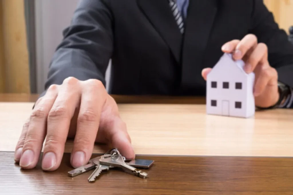 Um consultor de consórcio entrega as chaves e um modelo de casa a um cliente, ilustrando a realização do sonho da casa própria. A imagem é relevante para o tema de qual o melhor mês para dar lance em consórcio.