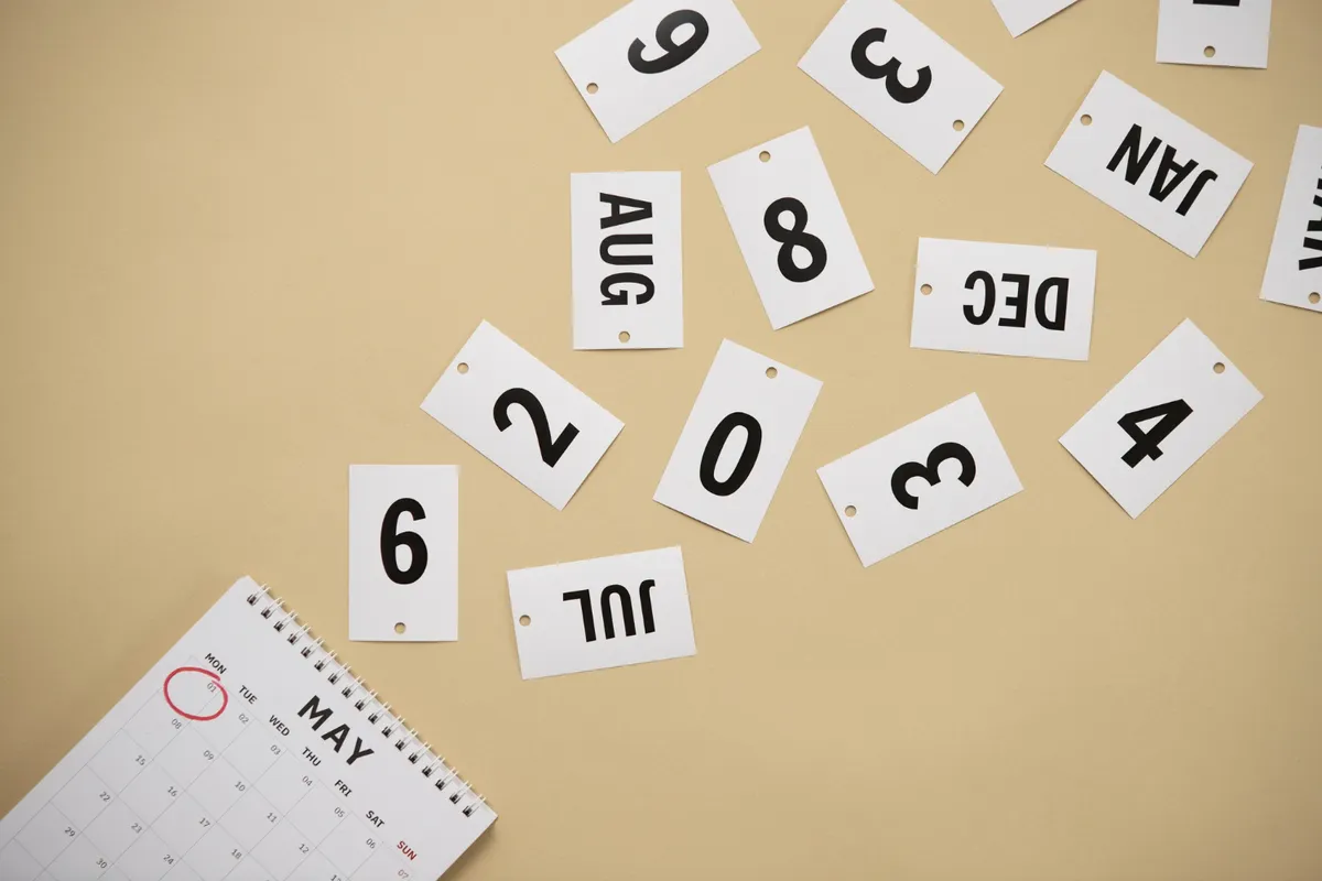 Um calendário com o mês de maio marcado e várias fichas com meses e números espalhadas, representando o planeamento e a estratégia de escolher o melhor mês para dar lance em consórcio.