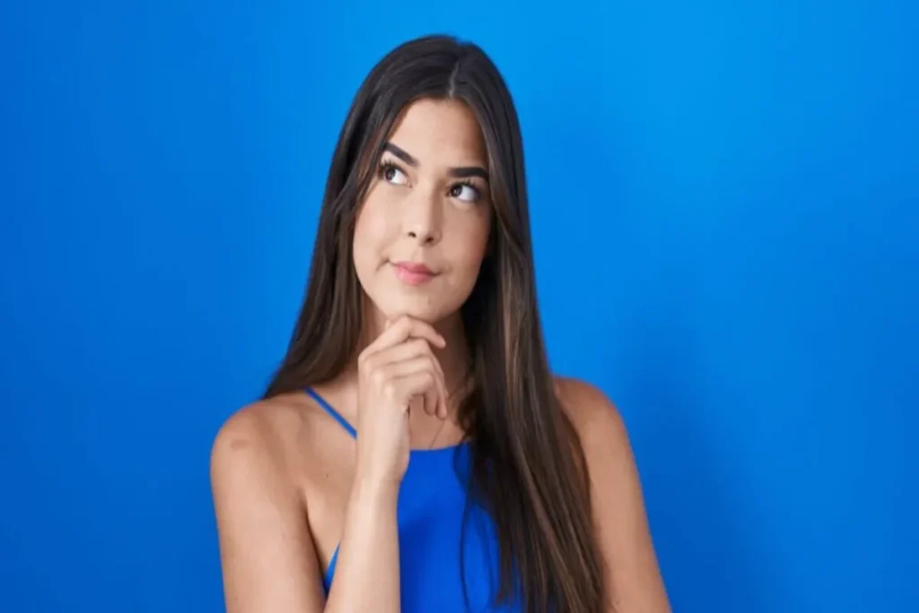 Mulher morena com expressão pensativa, refletindo sobre nome sujo, com a mão no queixo e um fundo azul.