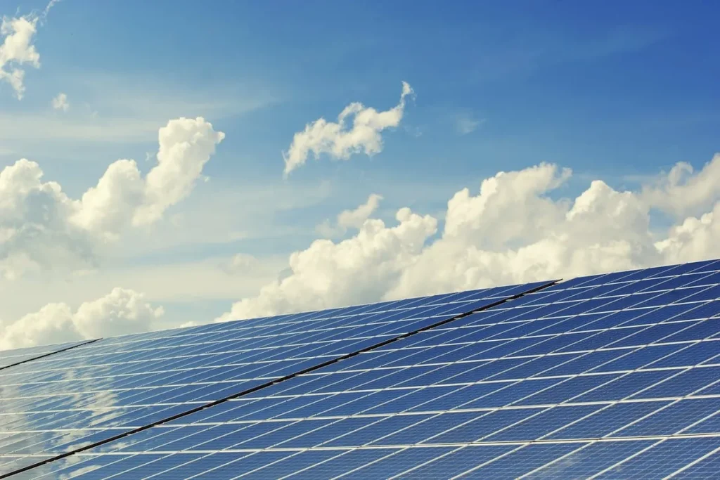 Painéis solares azuis instalados ao ar livre, refletindo a luz do sol sob um céu azul claro com nuvens brancas esparsas.