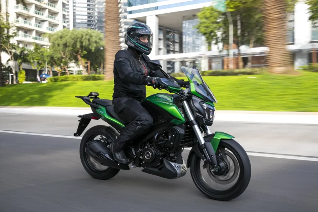 Pessoa de capacete e vestimenta de segurança pilotando motocicleta esportiva verde em estrada urbana com palmeiras.